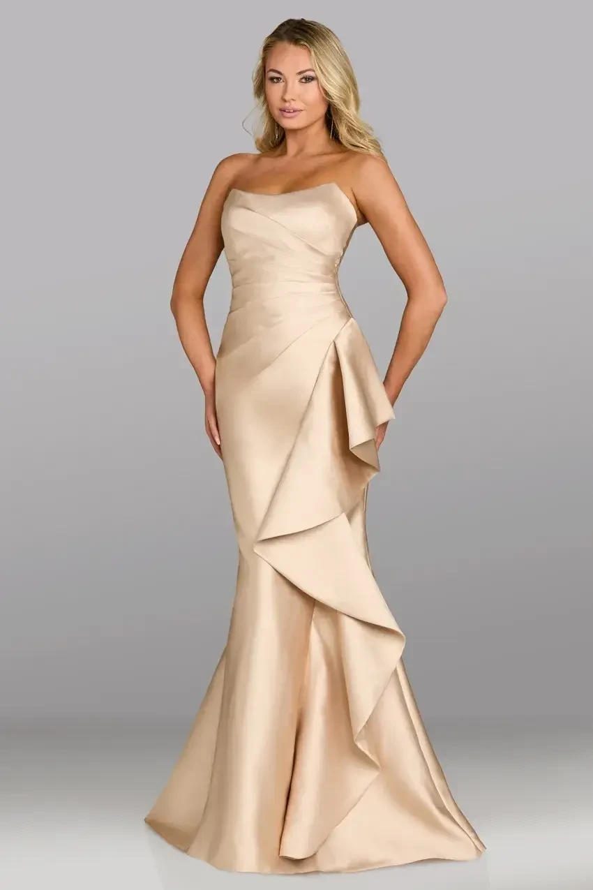 Woman in an elegant, strapless beige gown with cascading ruffle accents poses confidently. The background is a simple gray, emphasizing her sophistication.