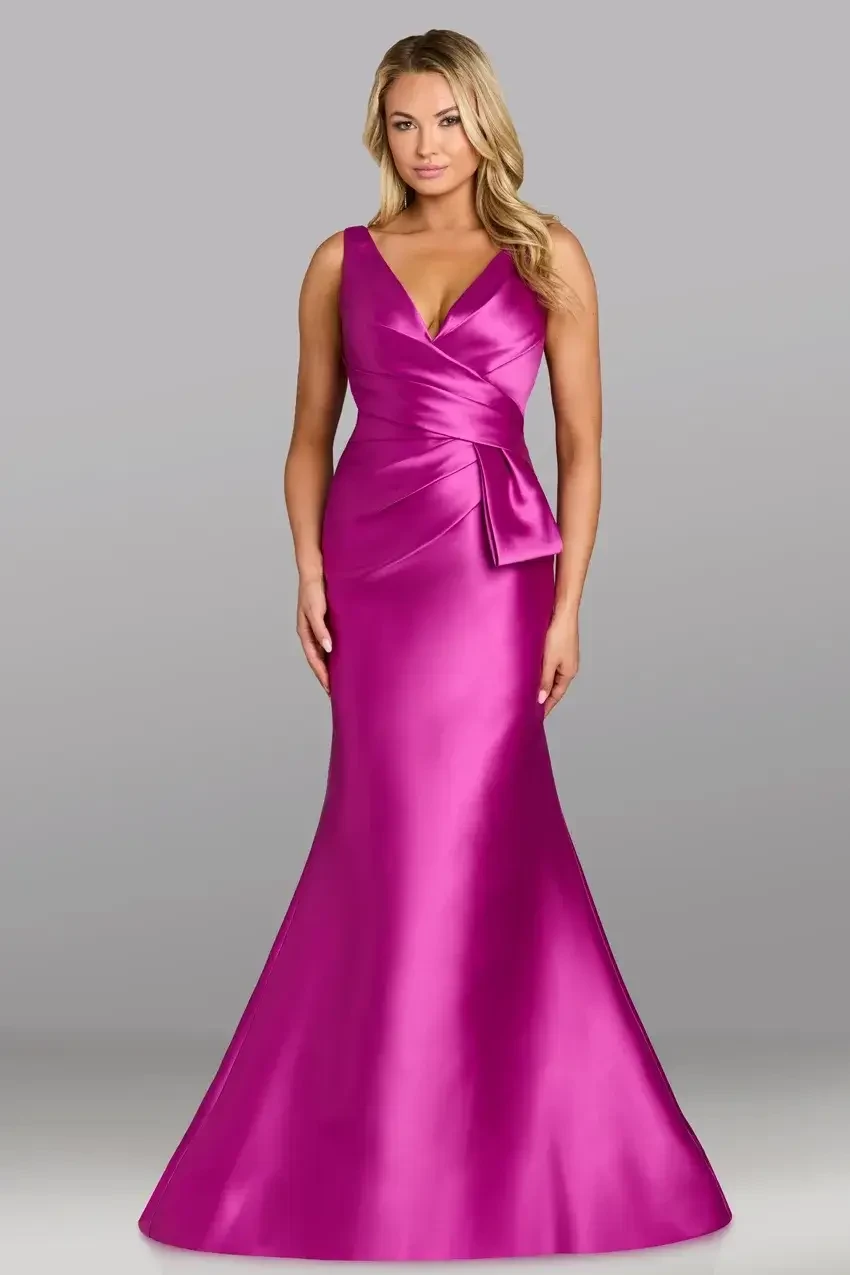 A woman in a vibrant magenta satin gown stands against a gray background. The dress features a V-neck, fitted waist with a bow, and a mermaid-style skirt.