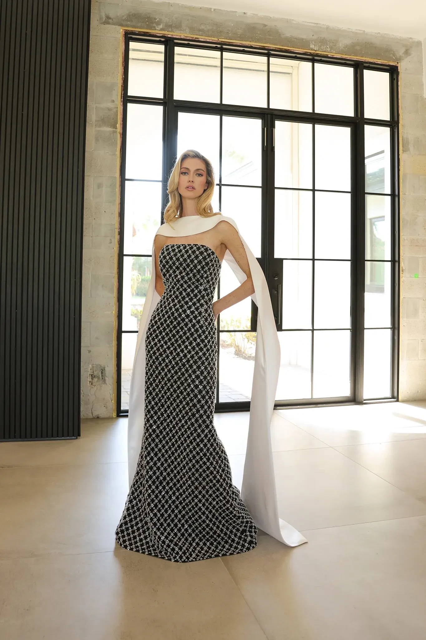 model is wearing a strapless floor length patterned evening gown with a long  neck scarf