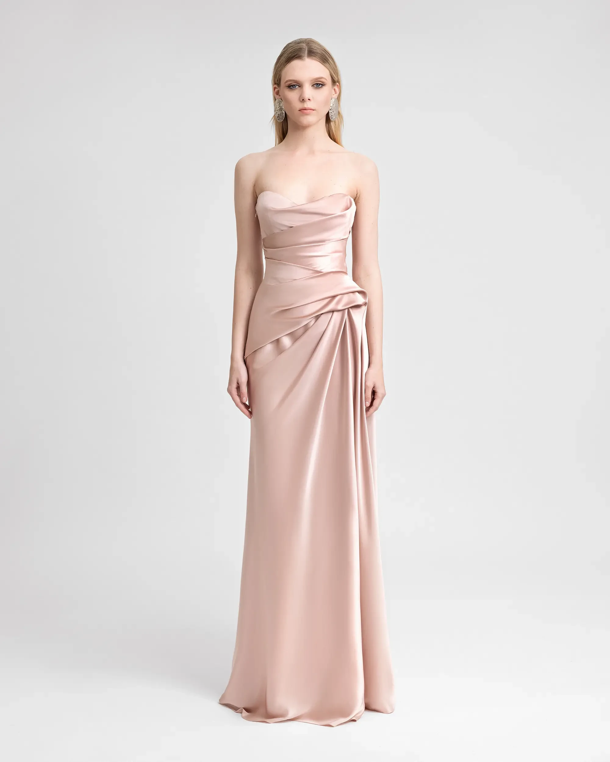 Model is wearing a light pink strapless sheath wedding dress with delicate ruching on the side 