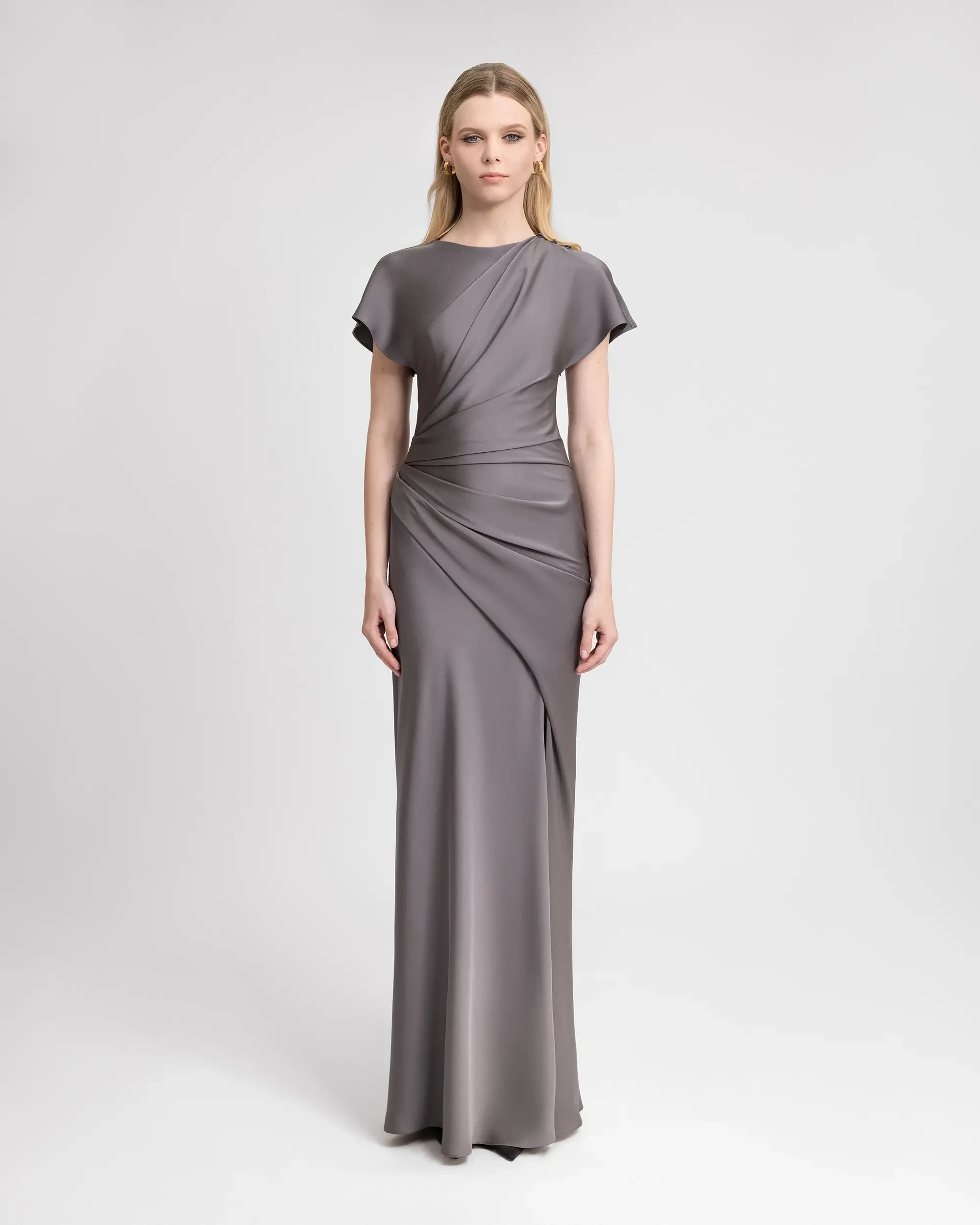 Model is wearing a dark grey high neckline short sleeve floor length evening gown with ruching down the side