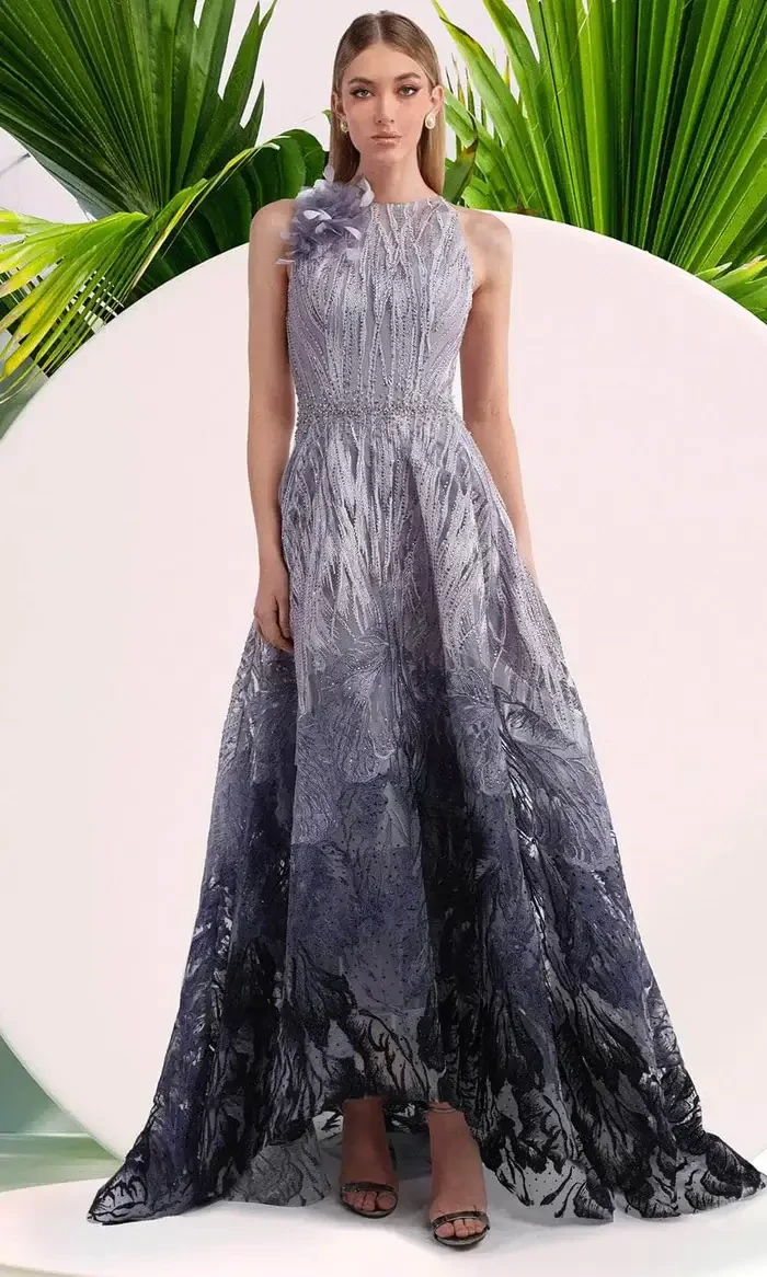 Woman in an elegant, floor-length, shimmering silver gown with a floral pattern poses confidently against a backdrop of lush green palm leaves.
