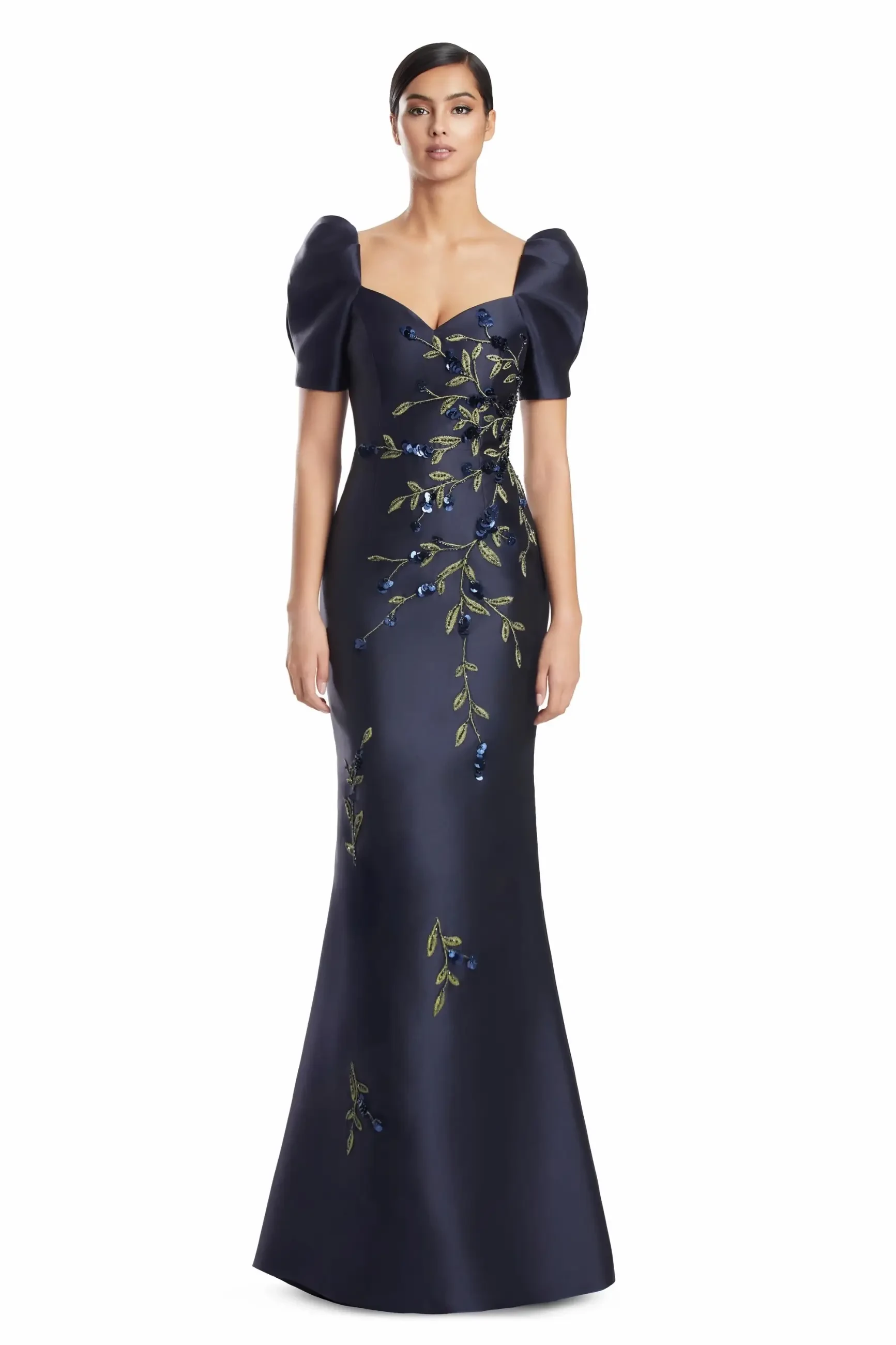 A model wearing a dark navy gown with short puff sleeves and floral embroidery.